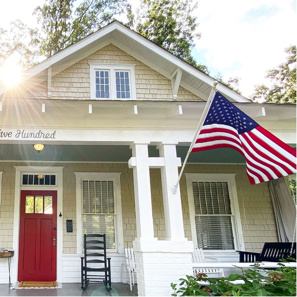 Welcoming front porch of historic home with colorful red front door and the American flag.
