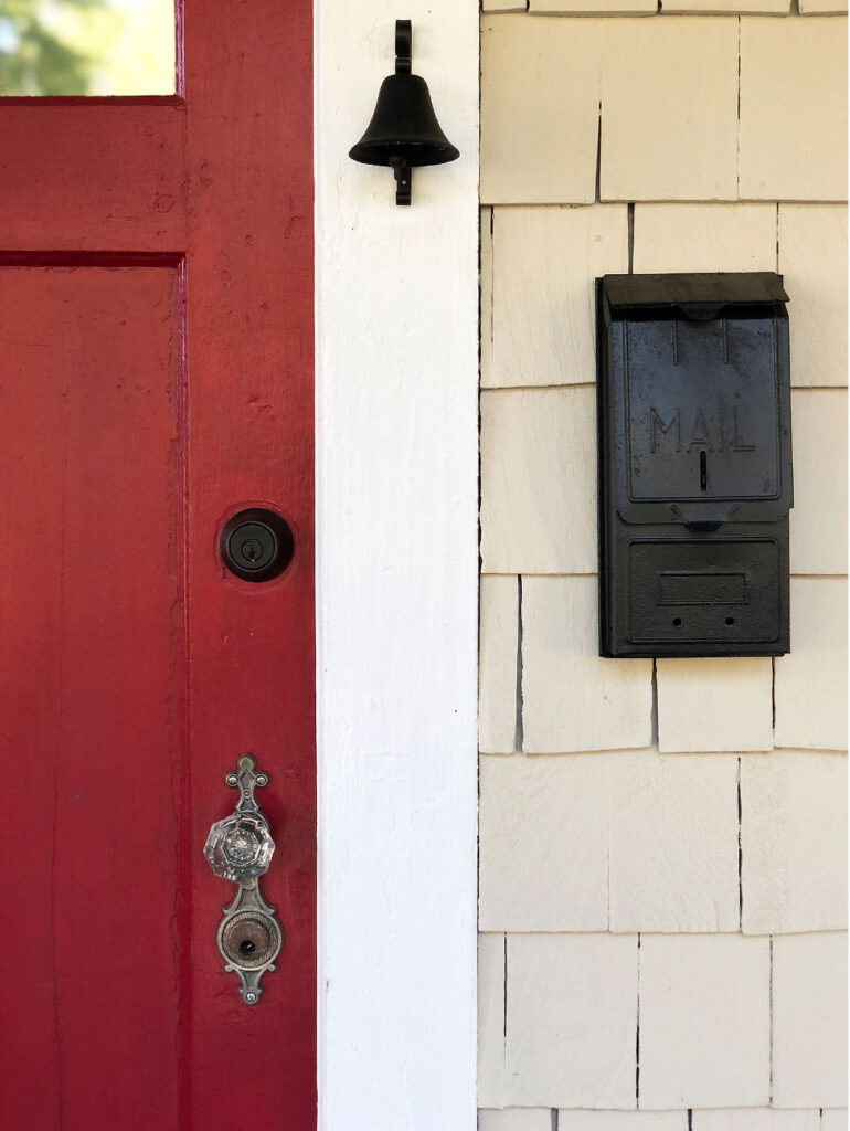 Red front door with vintage door hardware, mailbox, and door bell.