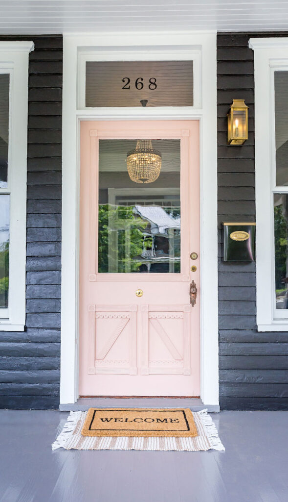 Queen Anne style historic home with black siding and soft pink front door.
